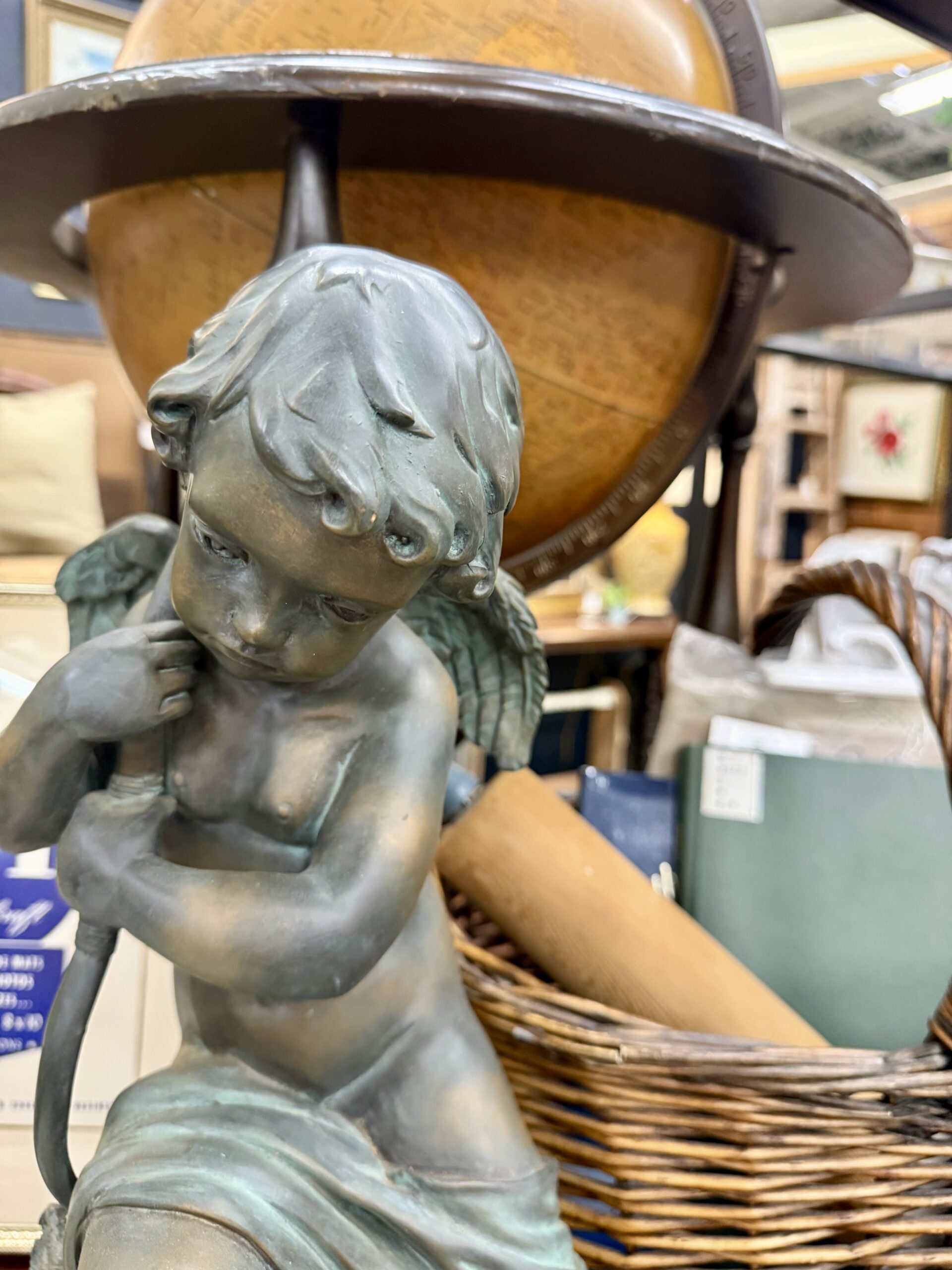 A decorative cherub statue with a vintage globe in the background flanked by a basket with books and a rolling pin inside.