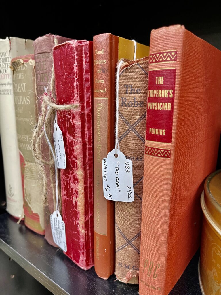 Collection of vintage hardcover books in red and brown tones with distressed covers and twine price tags.
