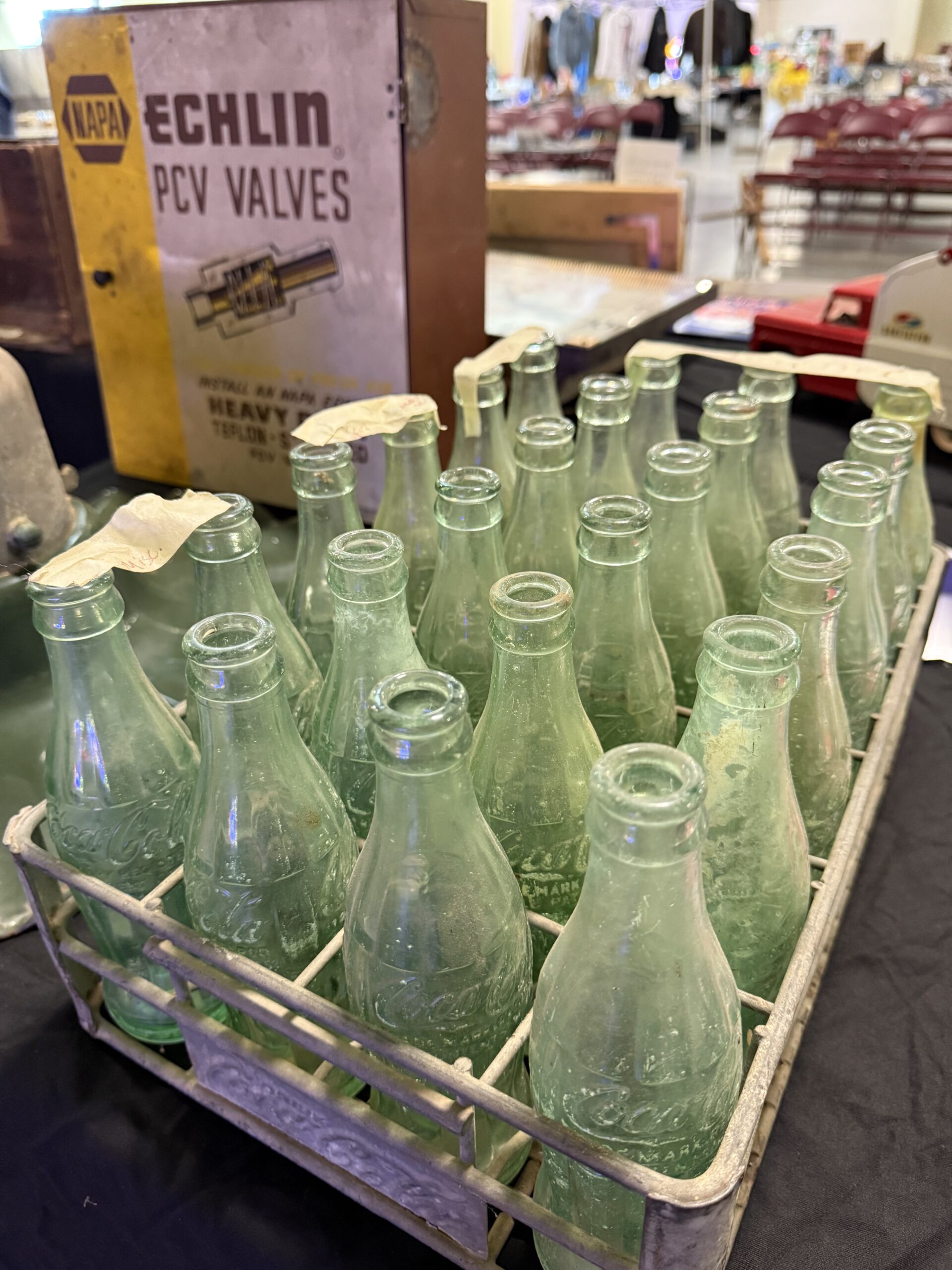 A vintage set of 24 green glass Coca Cola bottles in a metal crate at an auction.